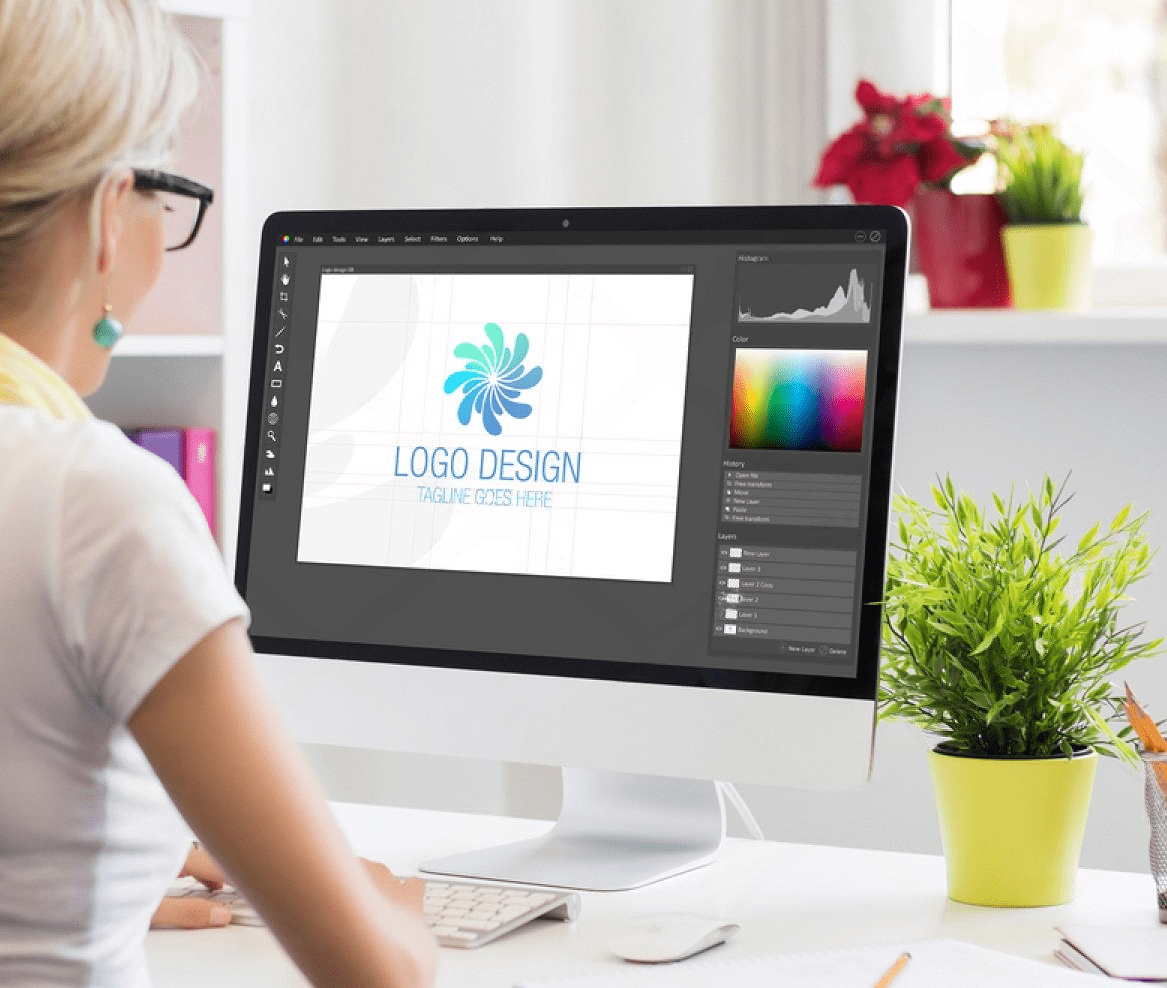 A woman designing a logo on her computer, surrounded by graphic design tools in a contemporary office.
