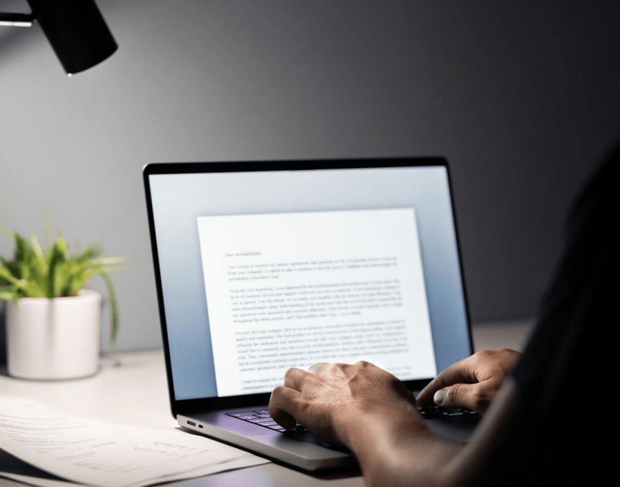 A person types content on a laptop in a dimly lit room, illuminated by the screen's glow at night.