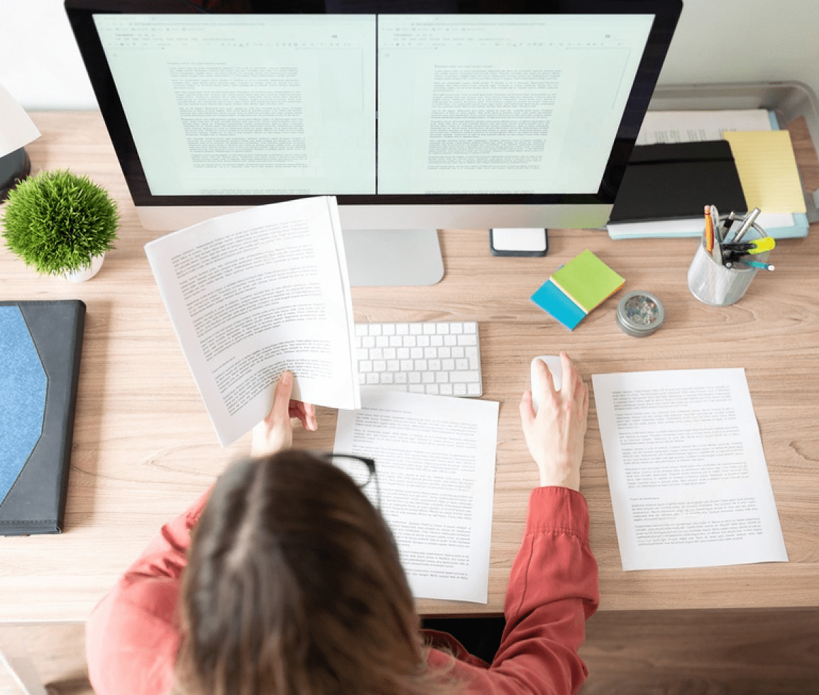 A woman is engaged with her computer at a desk, with content strategy documents and papers nearby.