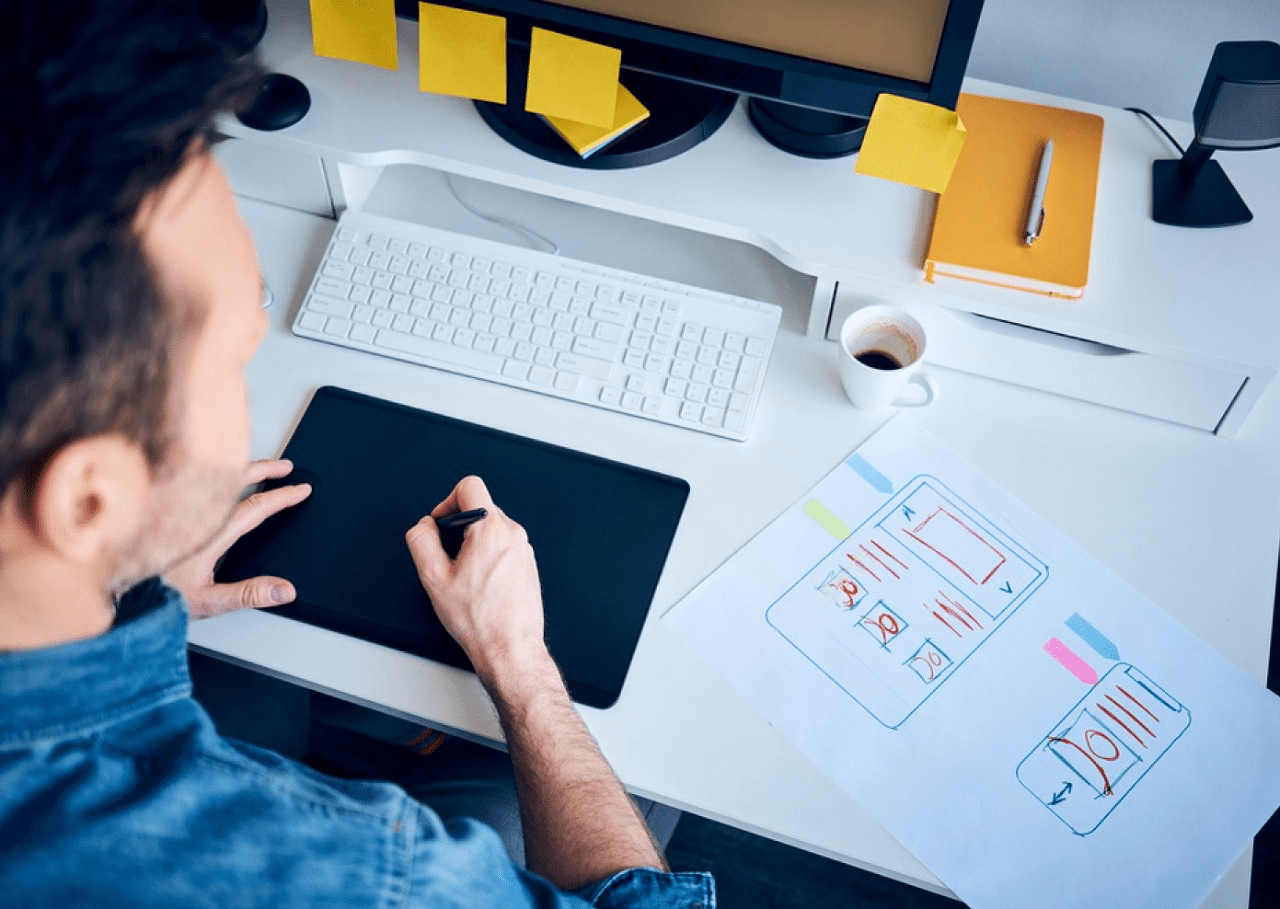 A man engages with his computer, using a pen and paper for responsive web design.