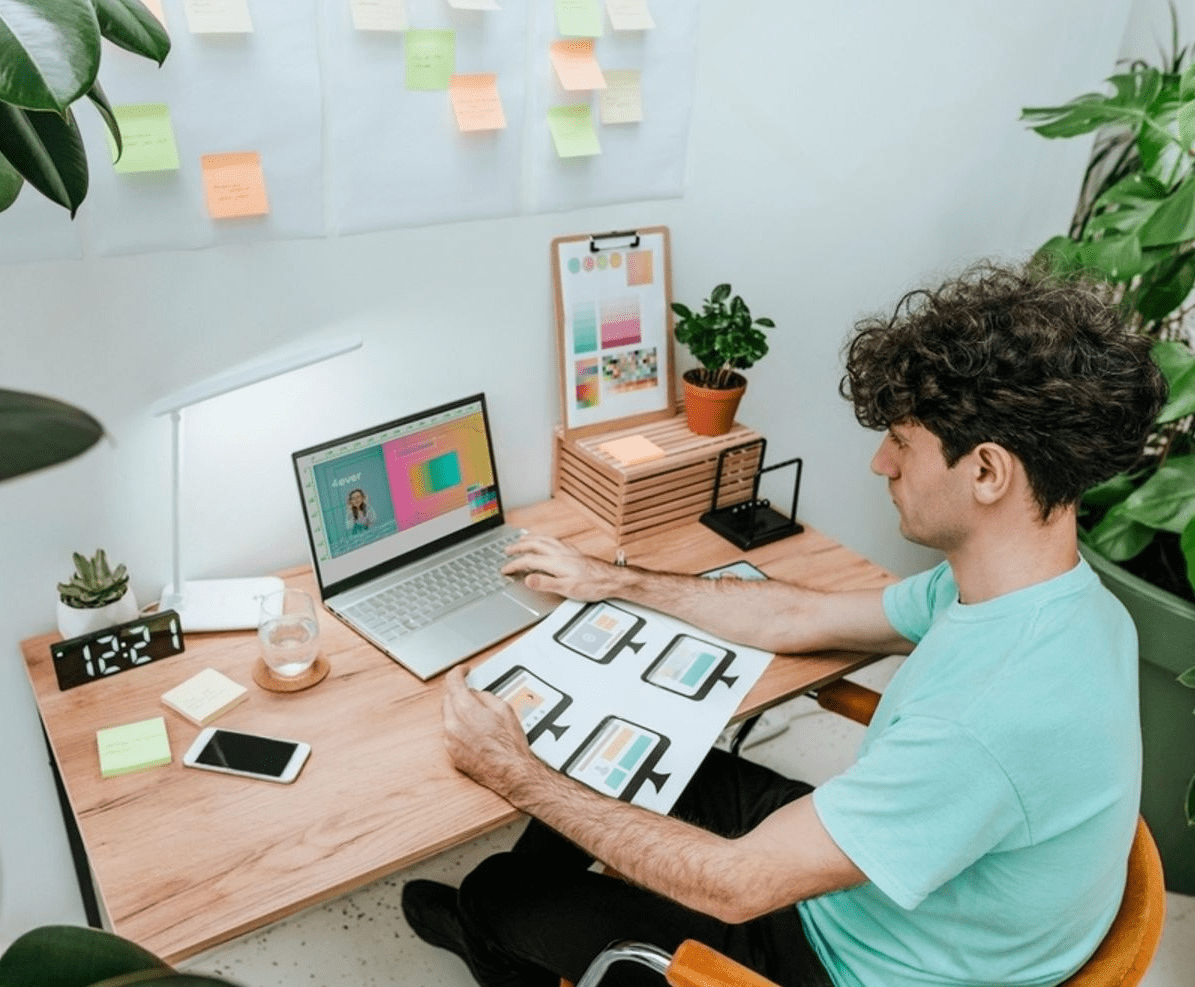 A man working at a desk with a laptop, accompanied by a plant, illustrating a blend of website development layout and nature.